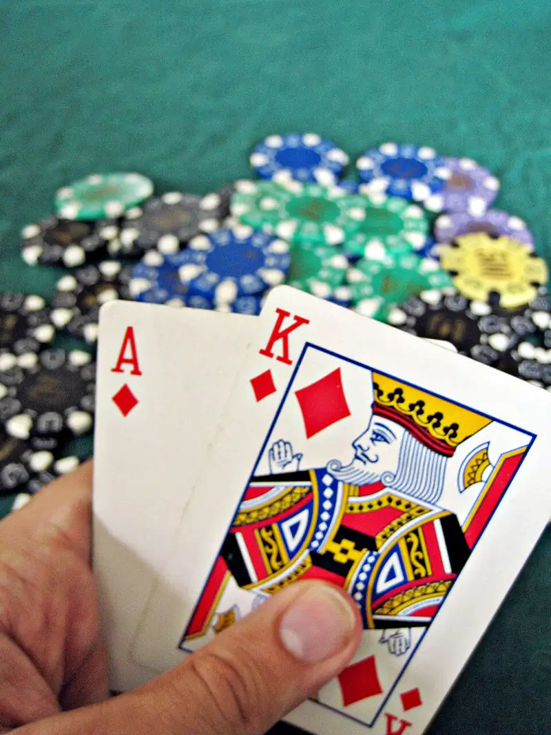 Ász és király egy kézben, mögötte zsetonok a posztón: blackjack