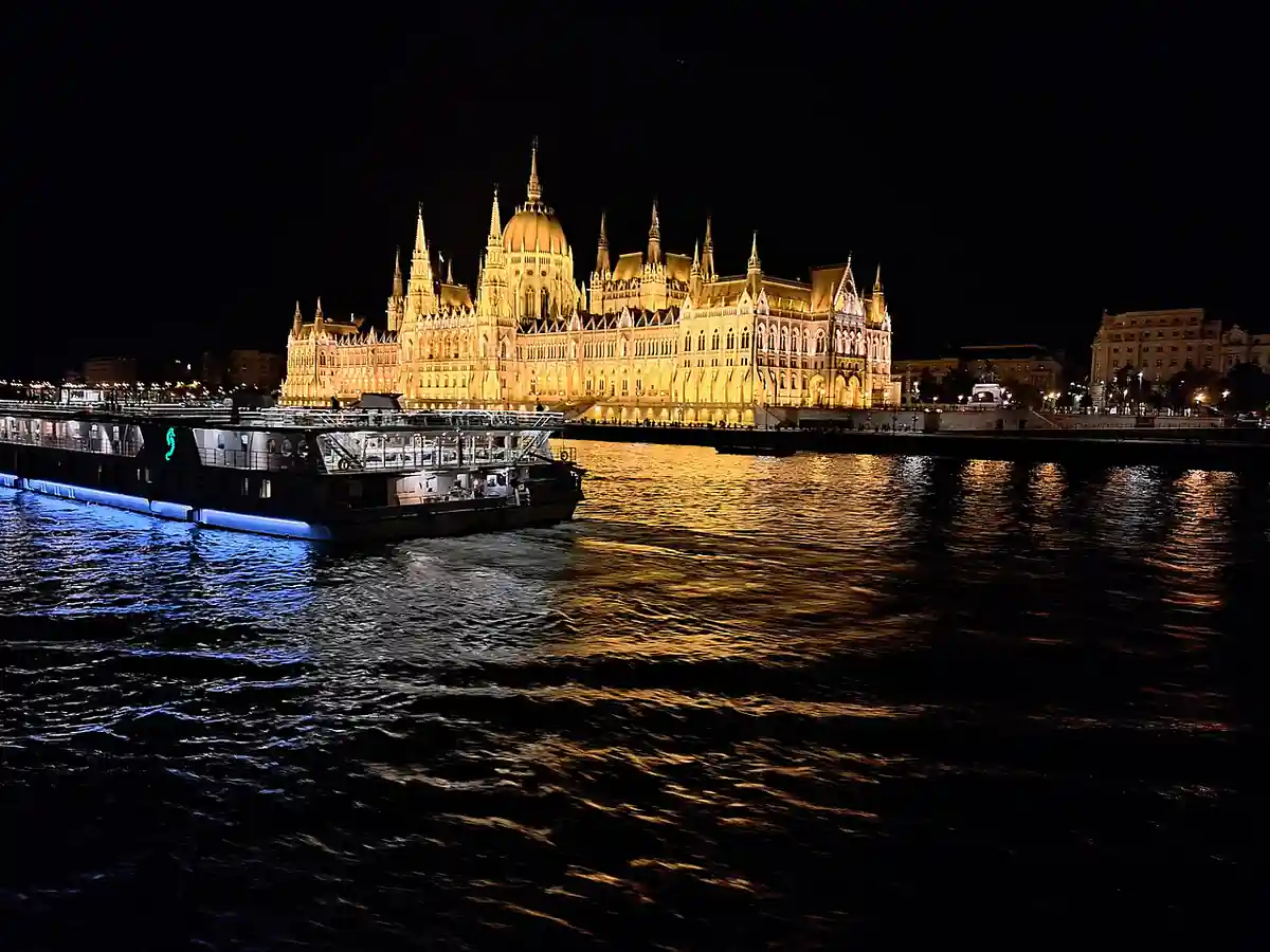 Kék fényekkel kivilágított sétahajók a Dunán, háttérben az Országház